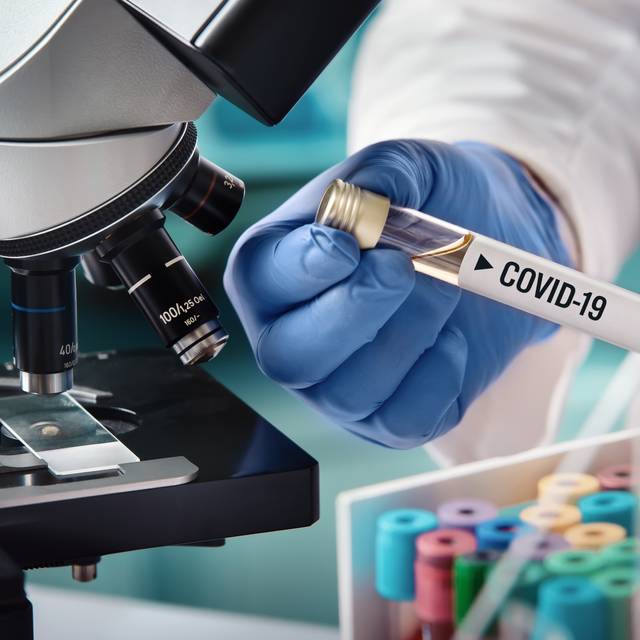 Microbiologe mit einer biologischen Probe, die mit dem Coronavirus kontaminiert ist. Auf der Probe ist das Etikett Covid-19 zu erkennen.