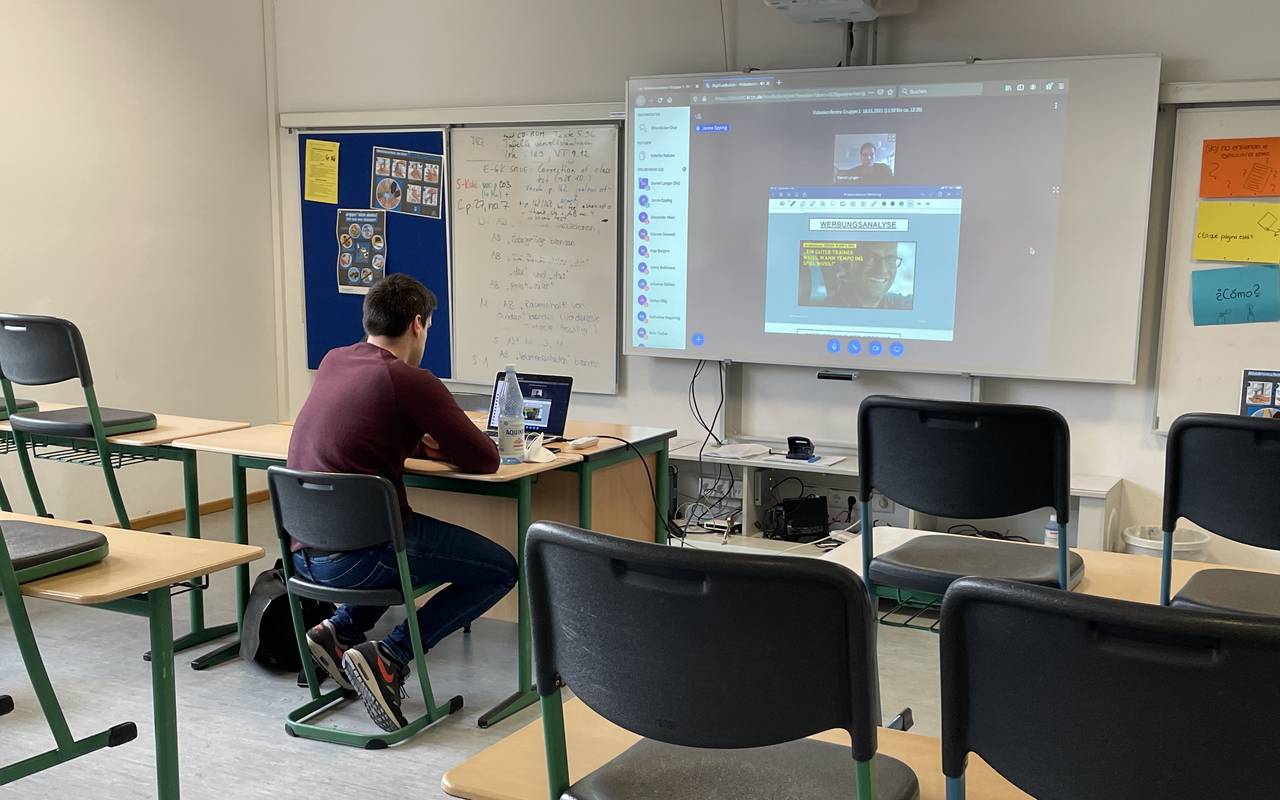 Homeschooling in der Coronazeit. Der Lehrer sitzt alleine im Klassenraum, die Schüler sitzen zuhause.
