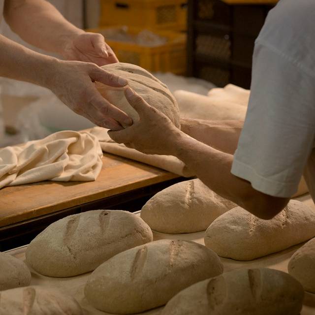 Hände reichen einen rohen Brotlaib jemand anderem zu.