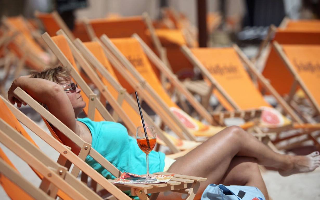 Eine Frau genießt mit einem Drink auf einem Liegestuhl die Mittagssonne am Stadtstrand.. Foto: Daniel Karmann dpa/lby