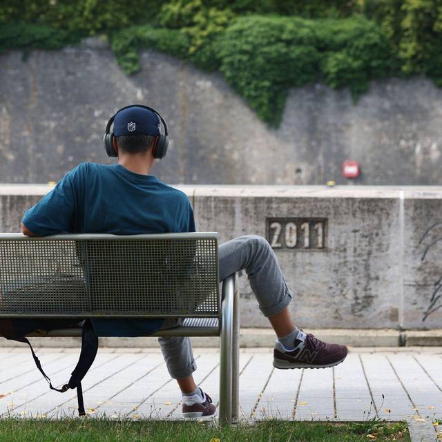 Junger Mann sitzt mit Kopfhörer auf einer Bank