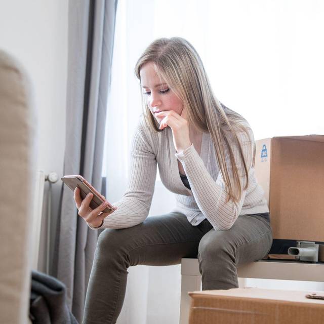 Eine Frau sieht zwischen Umzugskartons auf ein Handy