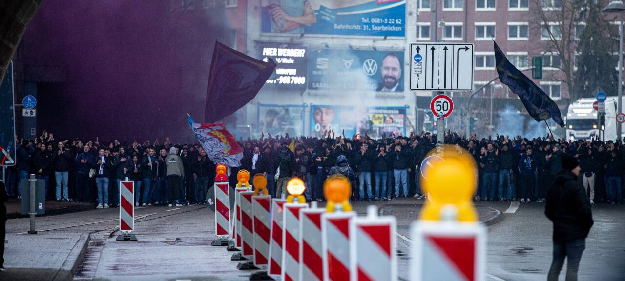 Fußballfans stehen in einem Tunnel und werden von Polizisten begleitet.