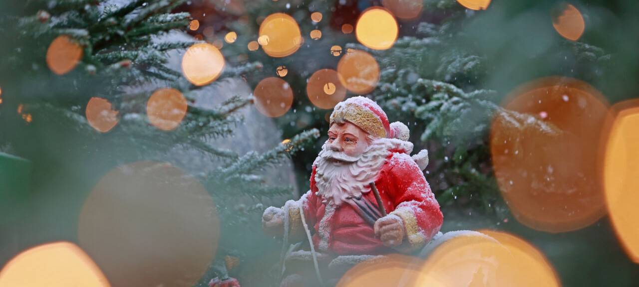 Blick durch eine Lichterkette auf eine schneebedeckte Weihnachtsmannfigur