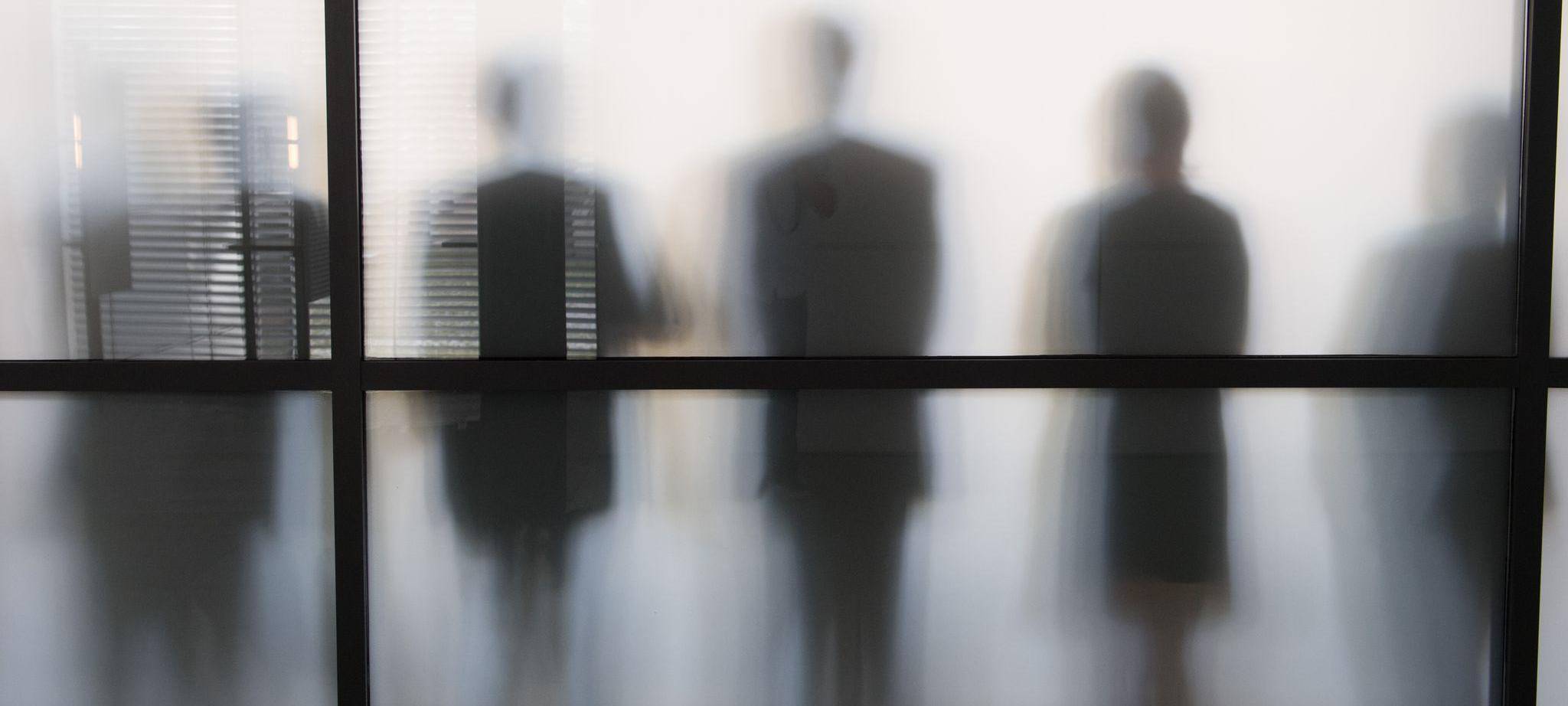 Personen stehen hinter eine Glasscheibe in einem Büro