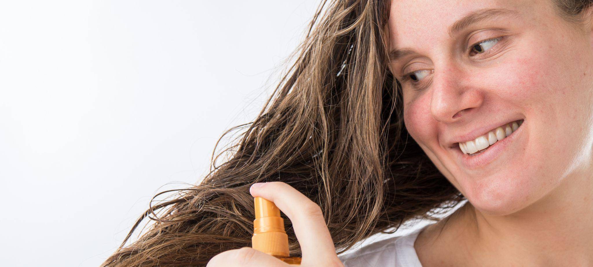 Eine Frau sprüht sich mit einem Haarpflegeprodukt auf die Haare
