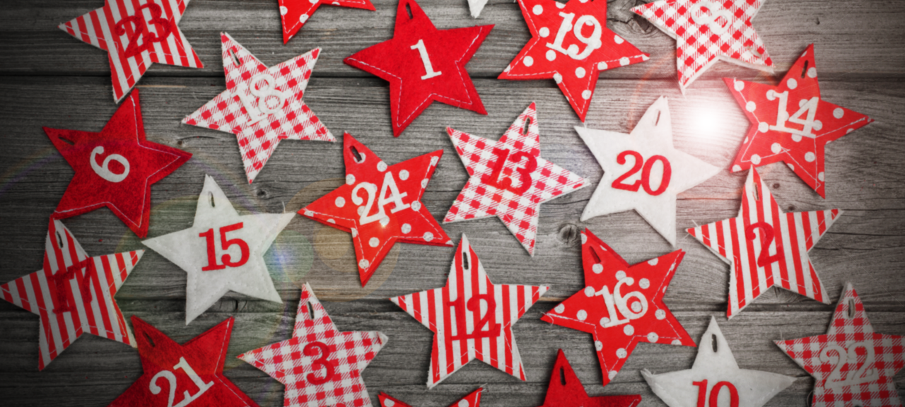 Rote und weiße Geschenktüten mit Nummerierungen der Adventskalendertage liegen auf einem Tisch und sind von oben fotografiert.